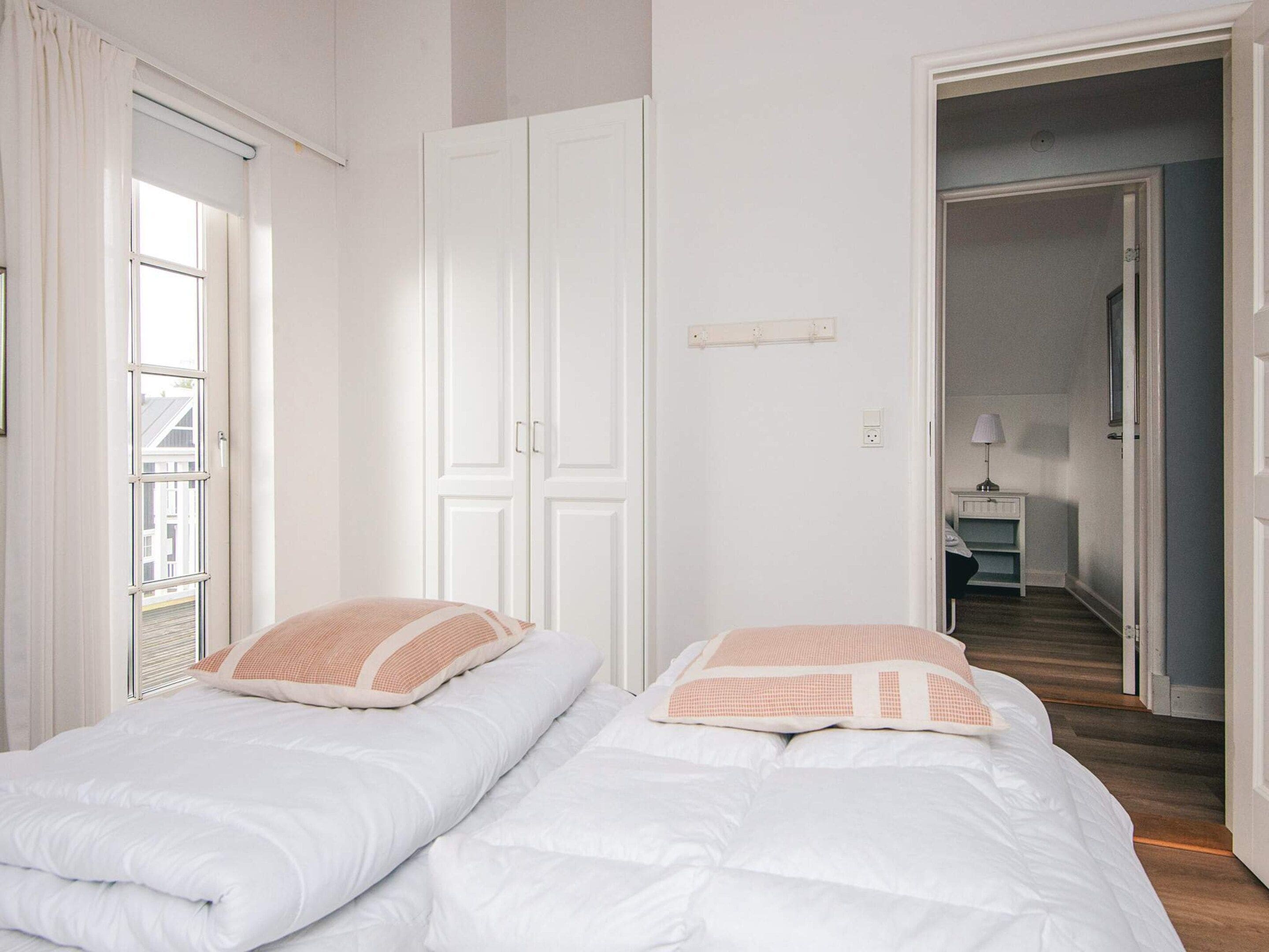 Una habitación con dos camas, un armario, una ventana y una puerta que da a otra estancia.
