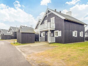 Een rij donkerhouten huizen met witte hekwerken, een geplaveid pad en een gazon.
