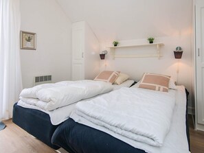A double bed with white and beige bedding, a bedside table with a lamp, and a small shelf with plants. - 8 Person Holiday Home in Gjern-by Traum (Gjern)