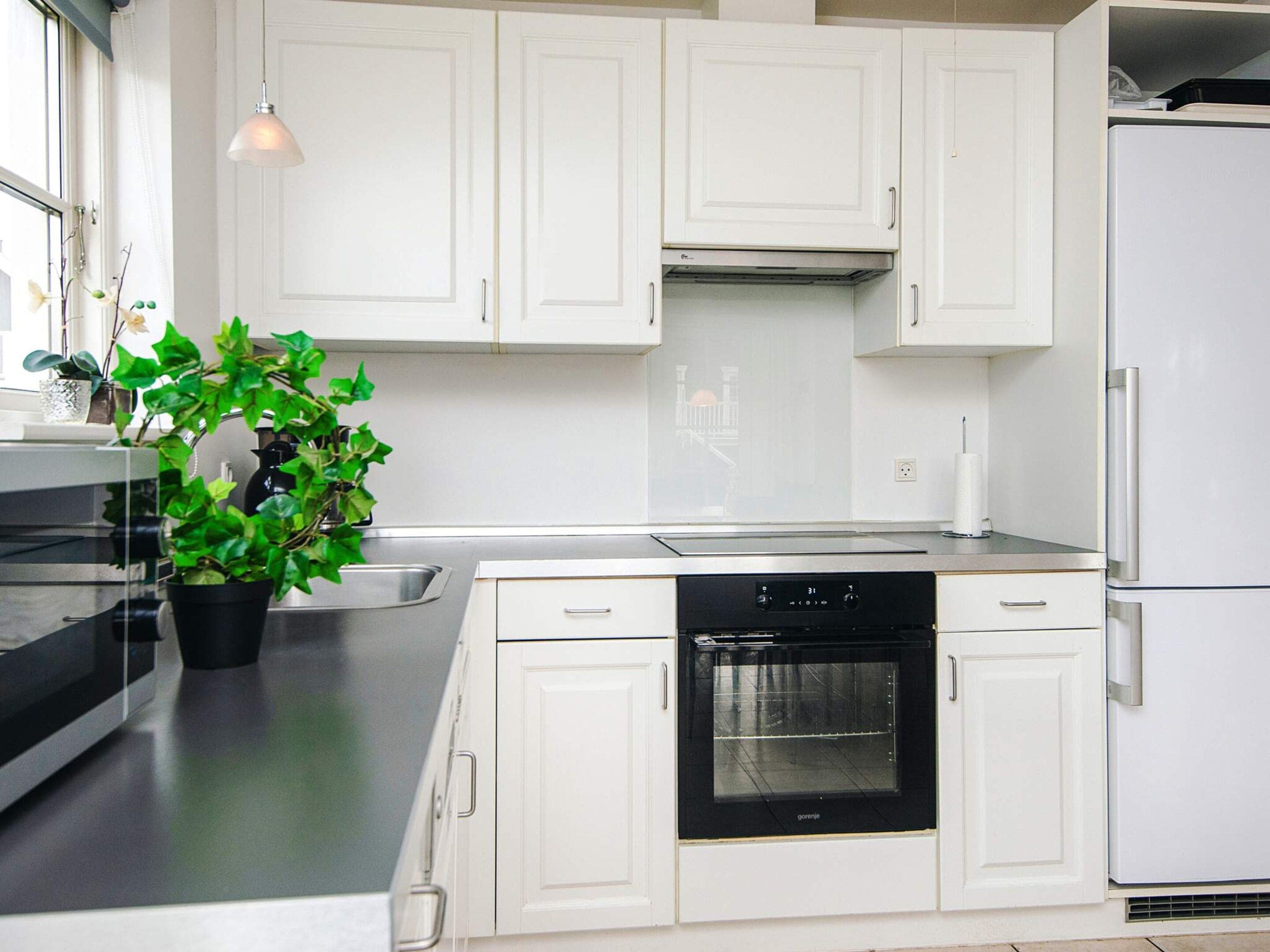 Una cocina moderna con armarios blancos, un horno negro y una planta en maceta.