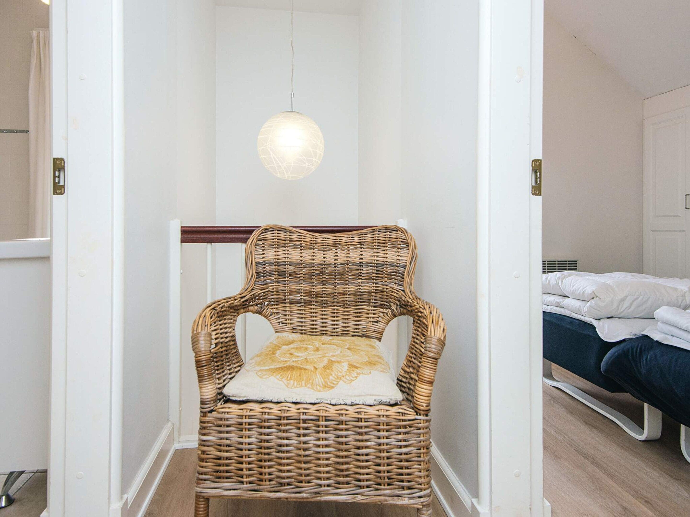 Una silla de mimbre con cojín en un pasillo que conduce a un dormitorio con cama.