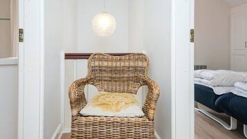 Una silla de mimbre con cojín en un pasillo que conduce a un dormitorio con cama.