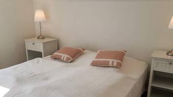 A bed with a white bedspread and two pillows, flanked by two nightstands with lamps.