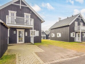 A row of dark wooden buildings with white railings and multiple windows, featuring a paved walkway and grassy areas. - 8 Person Holiday Home in Gjern-by Traum (Gjern)