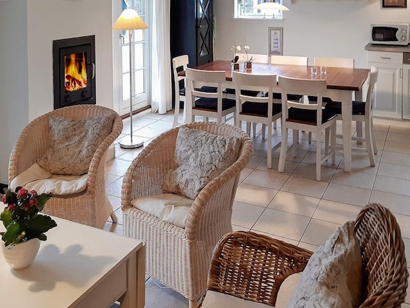 A cozy living room with wicker furniture, a fireplace, a dining table, and a kitchen area.