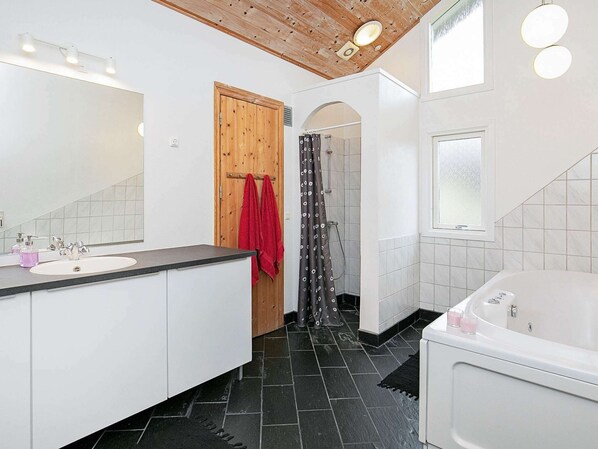 A modern bathroom with a wooden ceiling, a large mirror, a white sink, a bathtub, and a shower with a curtain.