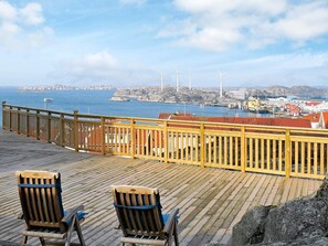 A wooden deck with two wooden chairs, overlooking a coastal town with wind turbines and buildings.