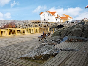Een houten terras met een stoel, een rotsachtige kustlijn en een wit gebouw met oranje daken op de achtergrond.