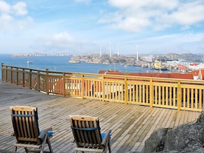 Een houten terras met twee stoelen, met uitzicht op een kustplaatsje met windmolens en een haven.