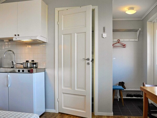 A compact kitchen with a white door, a sink, and a stove. There is a small dining area with a table and chairs. - Holiday Home in Rönnäng (Roennaeng)