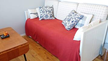 A room with a red sofa, white cushions, a wooden table with a candle, and a radiator.