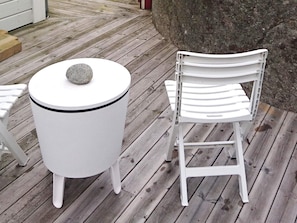 Een witte tafel met een steen erop, een witte stoel met een rugleuning en een houten terras.
