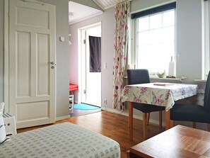 Une pièce comprenant un lit, une table avec des chaises, une fenêtre avec des rideaux et une porte donnant sur une autre pièce.