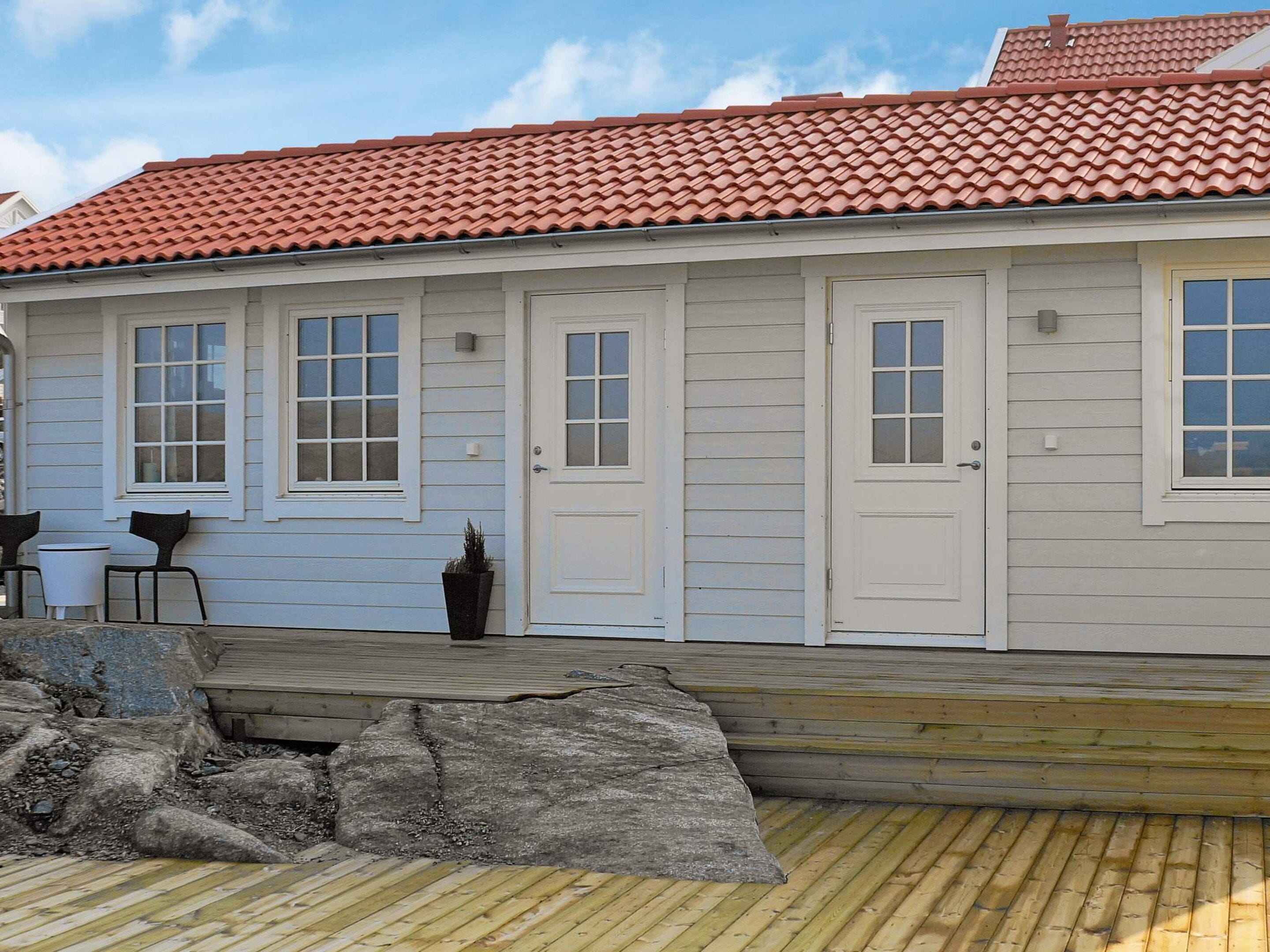 A building with a red-tiled roof, white exterior walls, and a wooden deck with a stone feature.