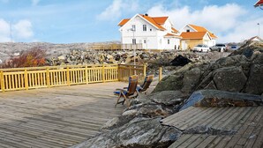 Eine Holzterrasse mit einem Stuhl, eine felsige Küstenlinie und ein weißes Gebäude mit orangen Dächern im Hintergrund.