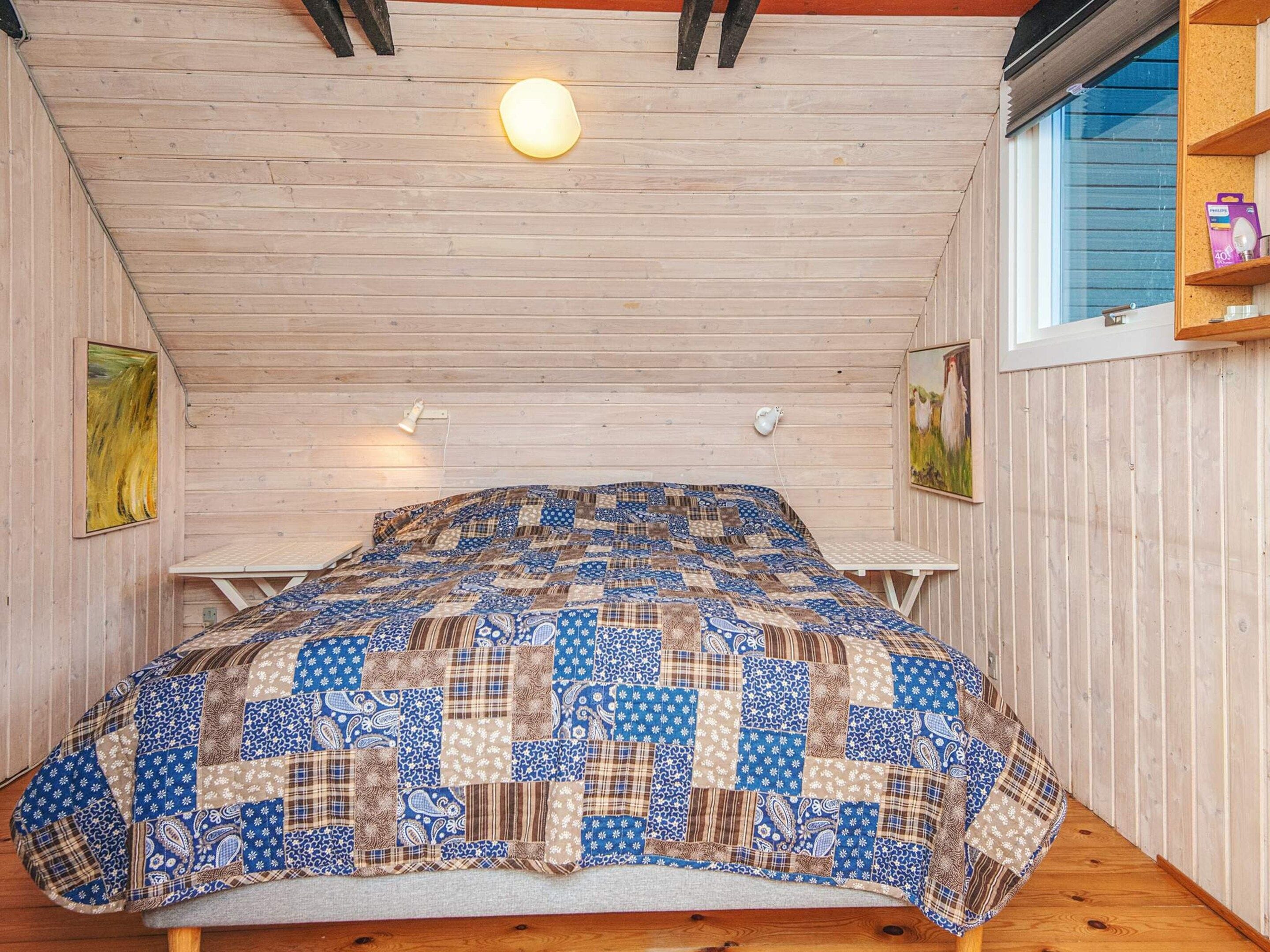 A small, cozy room with a wooden ceiling, a quilted bedspread, and a window with a view.