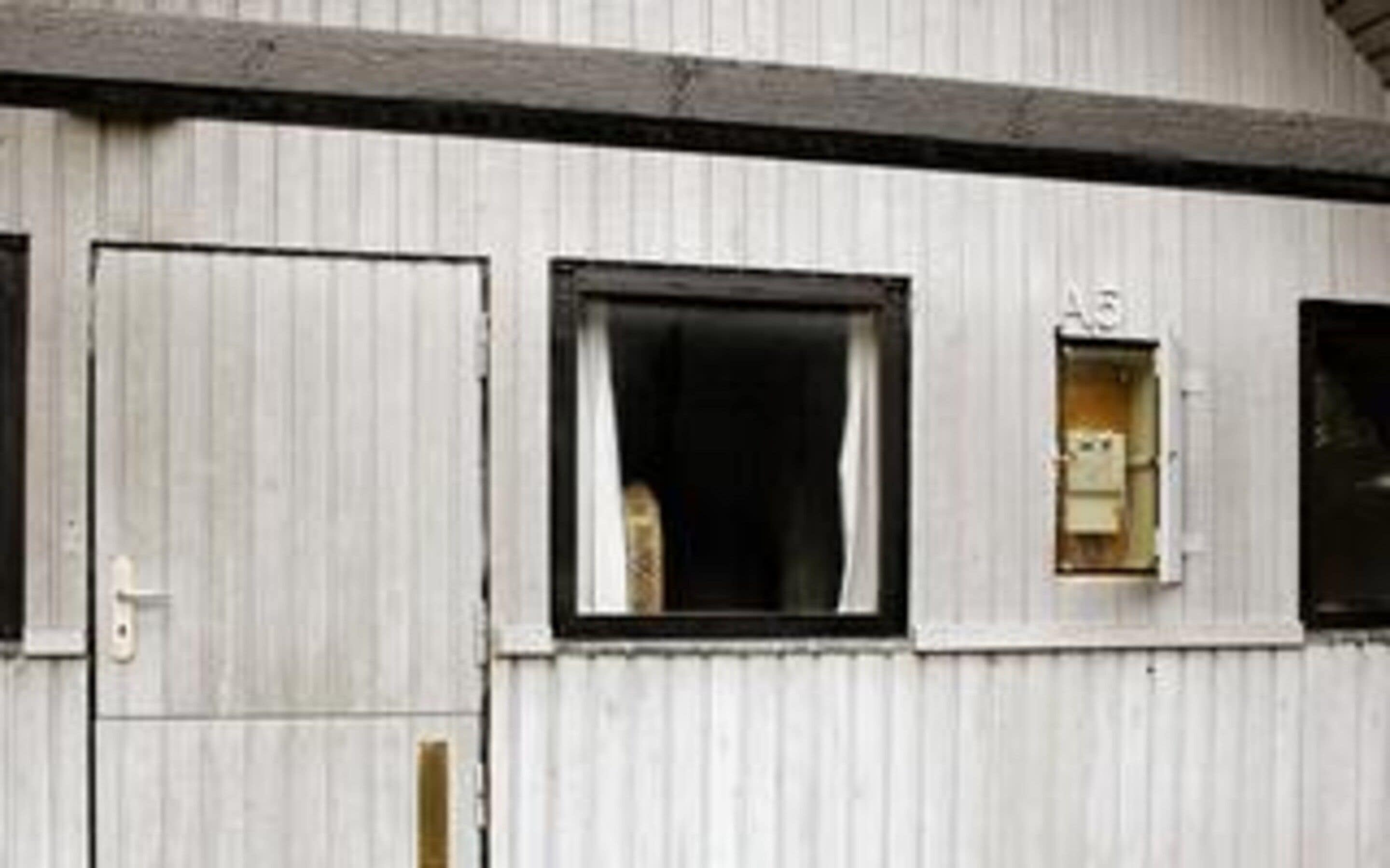 A building with a corrugated metal exterior, a closed door, and a window with a visible electrical box.