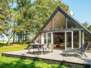 Ein modernes Haus mit einer großen Glasfassade, einer Terrasse mit Gartenmöbeln und einer Satellitenschüssel auf dem Dach.