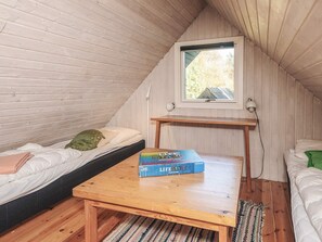 A cozy attic bedroom with a sloped ceiling, a window with a view, a wooden table, and two beds with pillows.