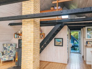 Ein Zimmer mit Kamin aus Backsteinen, Holzdielenboden, einer Treppe und Blick ins Freie.