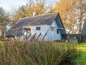A small, single-story building with a sloped roof, surrounded by tall grass and trees. - 6 Person Holiday Home in Fano (Fano)