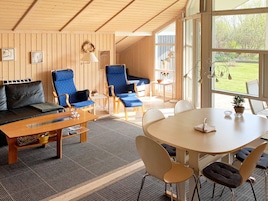 Una habitación acogedora con techo de madera, un sofá, sillas azules, una mesa de comedor y vistas a zonas verdes.
