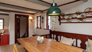 A dining area with a wooden table, bench seating, and a green pendant light. - Rustic Holiday Home in Løkken near Sea (Lokken)