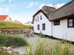A traditional white house with a thatched roof, stone wall, and a stone pathway leading to a wooden table and chairs. - Rustic Holiday Home in Løkken near Sea (Lokken)