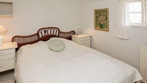 A bedroom with a wooden bed, a bedside table with a lamp, a wall-mounted picture, and a window with curtains. - Rustic Holiday Home in Løkken near Sea (Lokken)