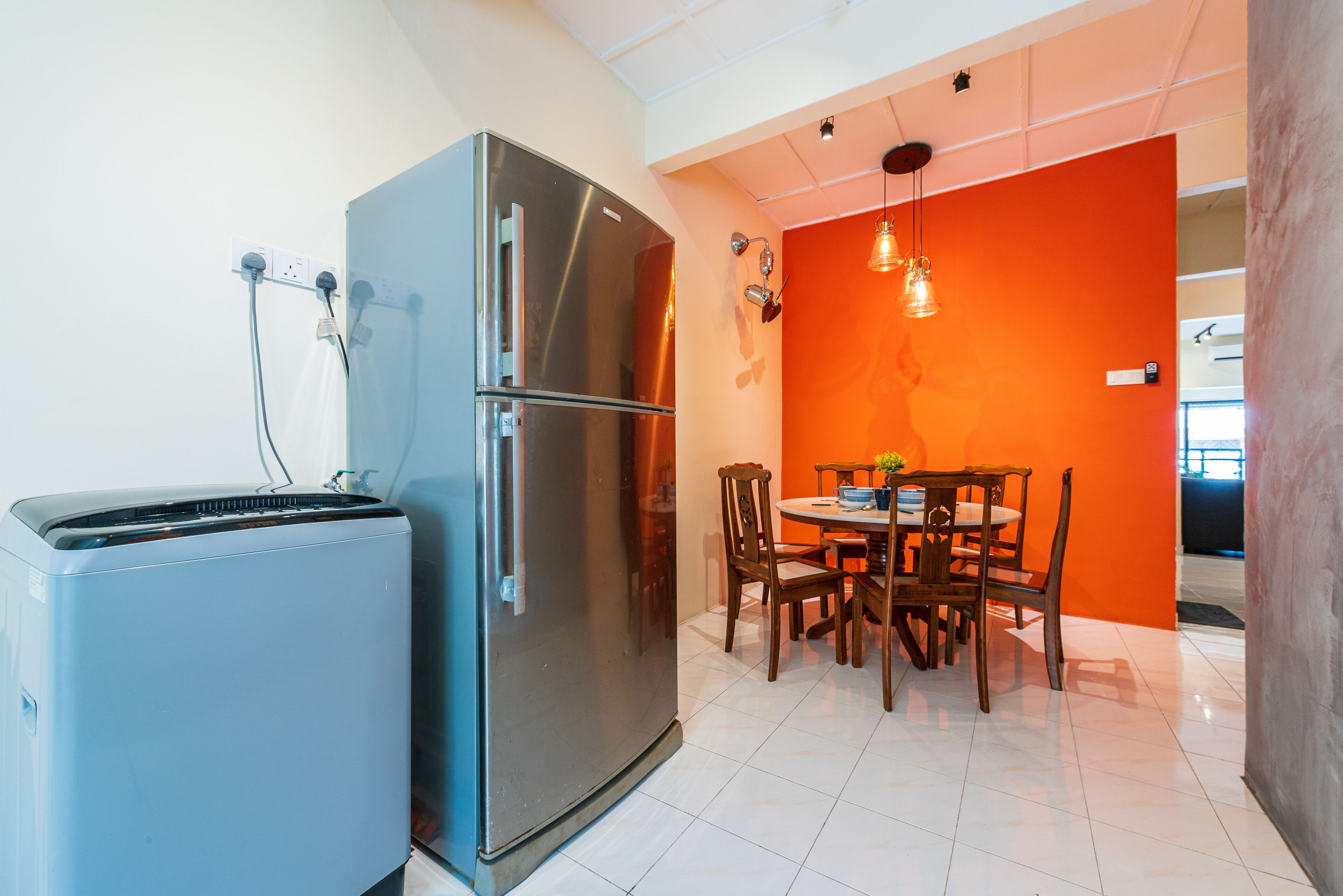 A compact kitchen with a modern stainless steel refrigerator, a small electric stove, and a dining area with wooden chairs and a table.
