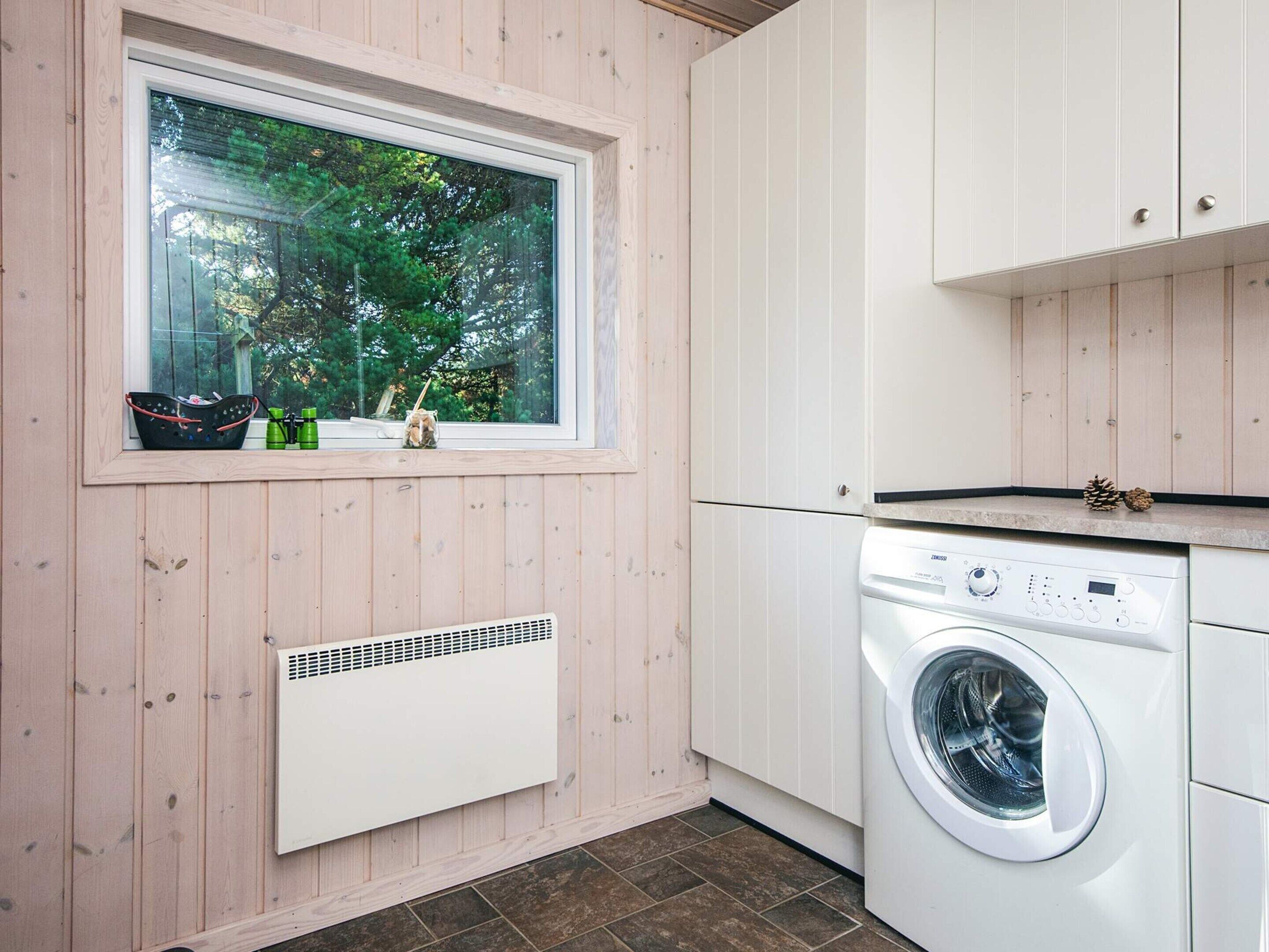 A compact kitchen with a built-in washer and dryer, a window with a view of trees, and a small window shelf with items.
