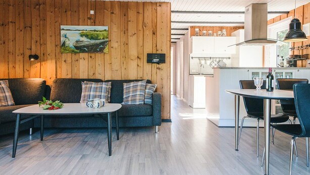 Ein modernes Wohnzimmer mit einer Holzvertäfelung, einer Couch, einem Couchtisch und einem Essbereich mit Tisch und Stühlen.