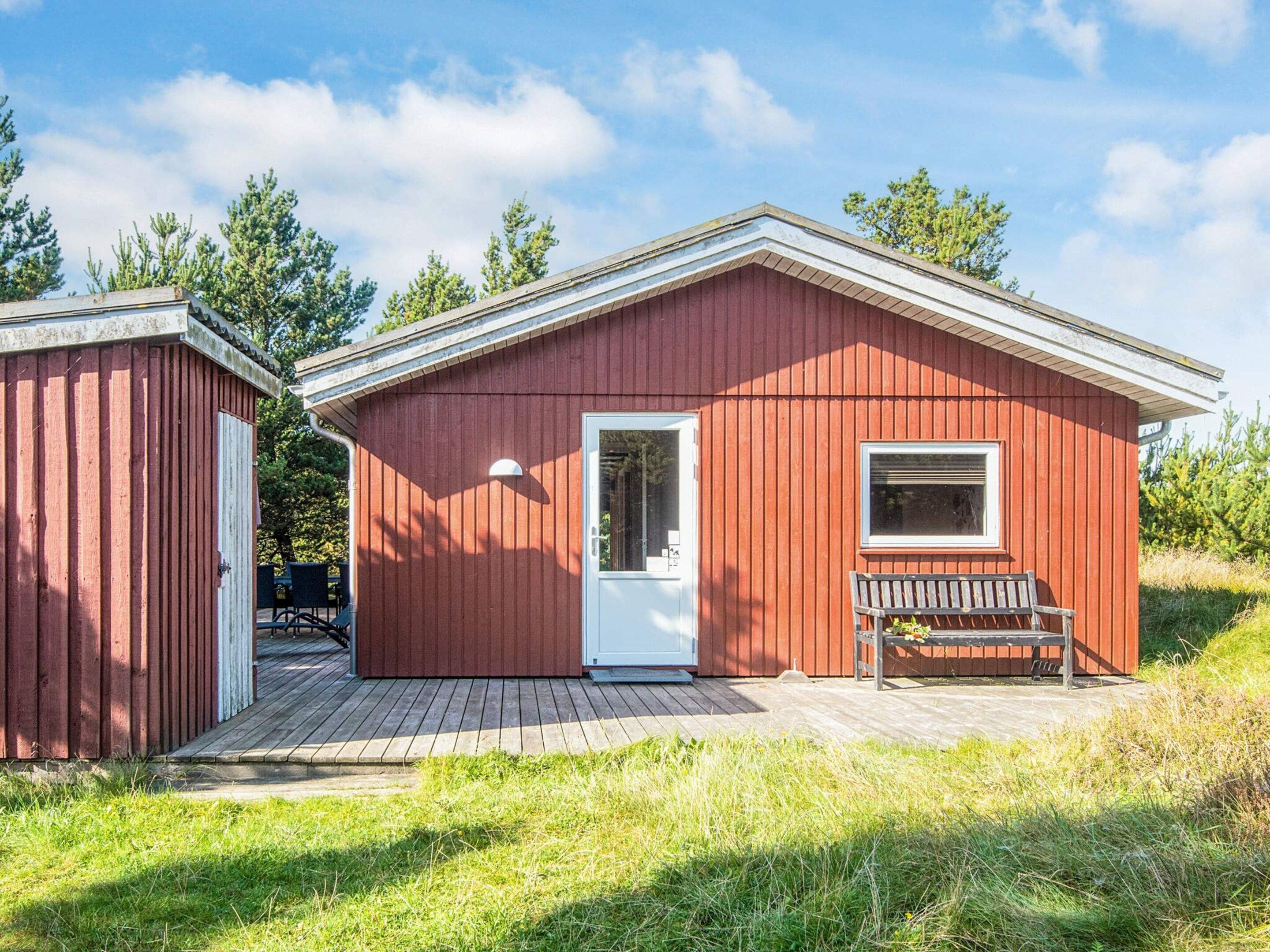 A red wooden cabin with a white door, a window, and a bench outside.