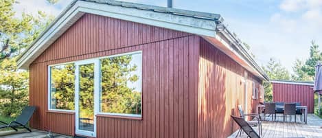 A wooden cabin with a large sliding glass door, a deck with outdoor furniture, and a chimney.