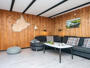 A cozy living room with a wooden wall, a sofa, a coffee table, and a fluffy rug.