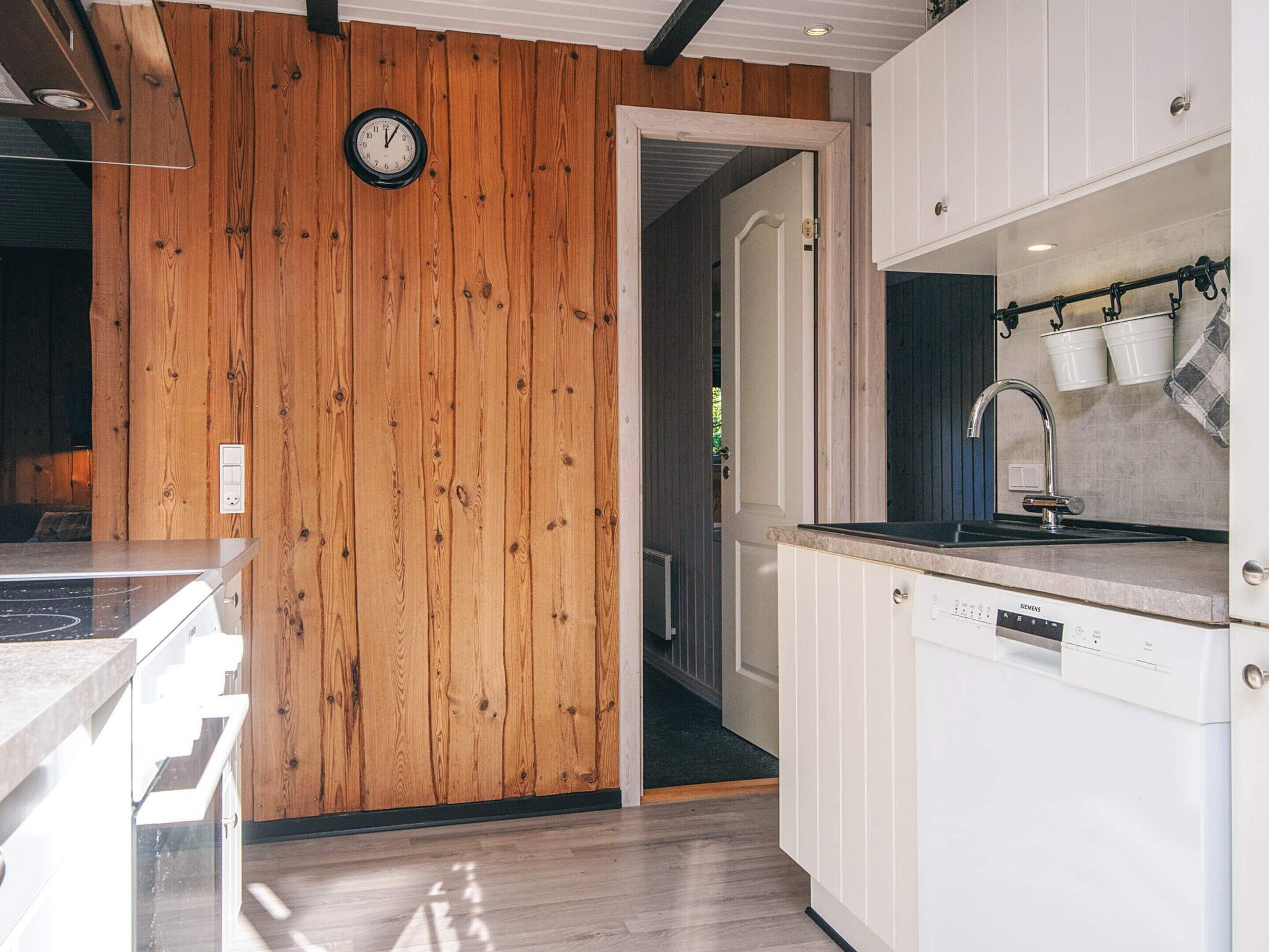 A modern kitchen with wooden paneling, a clock, and a Siemens dishwasher.