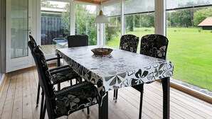 A covered patio with a table and chairs, large windows, and a view of a grassy yard. - Mesmerizing Holiday Home in Dannemare near Sea (Dannemare)