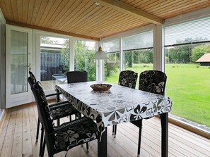 A covered patio with a table and chairs, large windows, and a view of a grassy yard. - Mesmerizing Holiday Home in Dannemare near Sea (Dannemare)