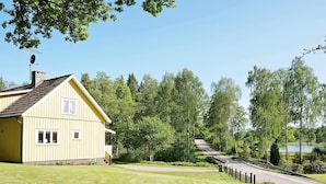 Une maison jaune avec un toit en pente, entourée d’une pelouse bien entretenue et d’arbres.