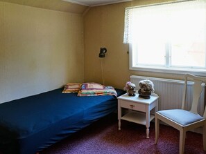 A room with a single bed, a small table with two decorative items, a chair, and a window with a curtain. - Holiday Home in Ullared (Ullared)