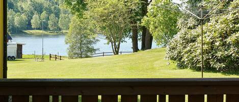 A view from a balcony overlooking a lake with trees, a wooden deck, and a small building.