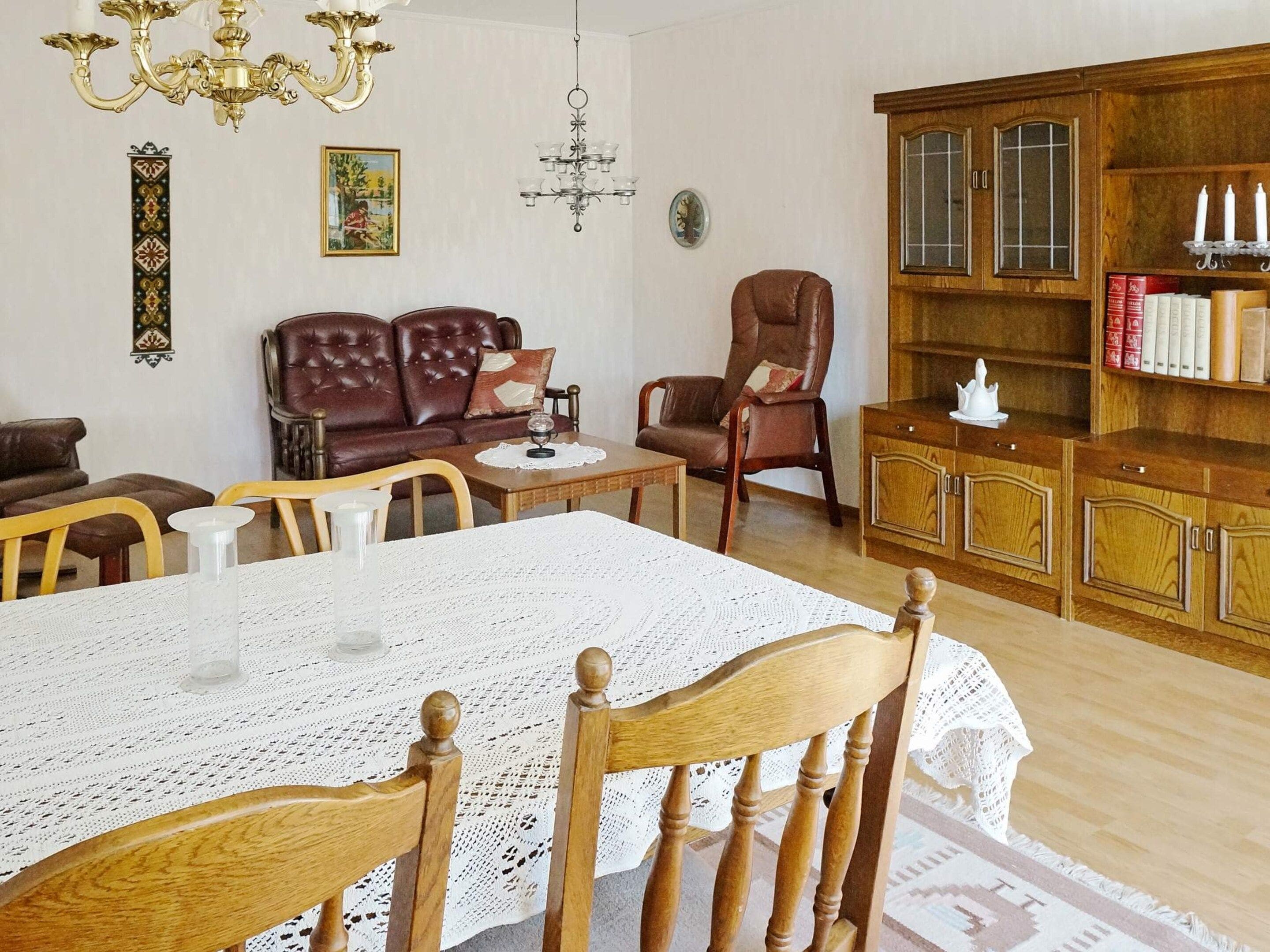 Ein gemütliches Wohnzimmer mit Esstisch, Ledersofas, einer Holzeinrichtung mit Büchern und einer Chandelier.