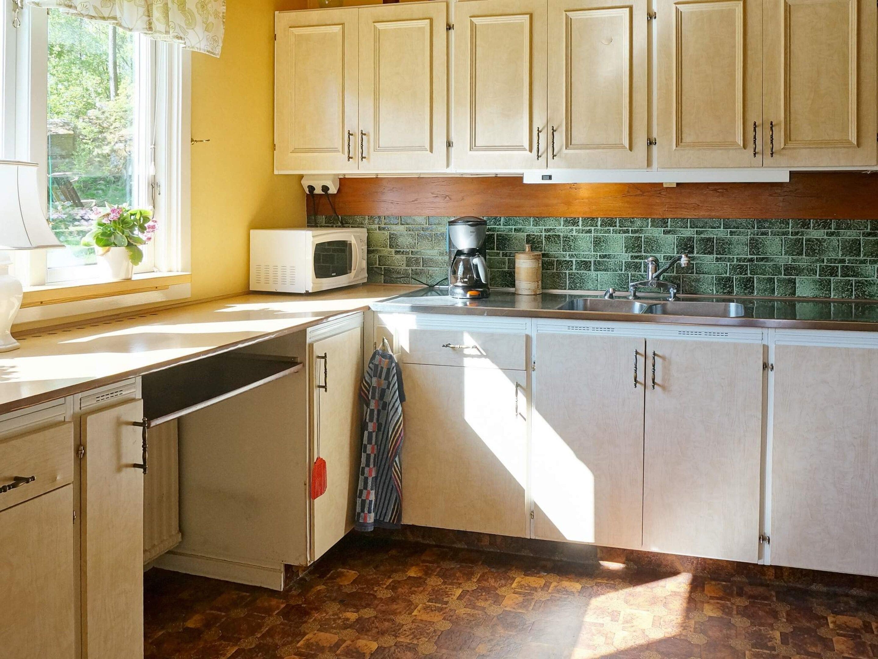 A kitchen with white cabinets, a microwave, a coffee maker, and a window with plants.
