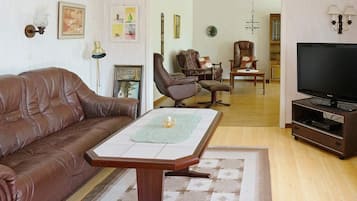 A living room with a brown leather sofa, a wooden coffee table, a television on a stand, and a patterned rug.