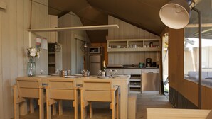 A spacious kitchen with wooden cabinets, a dining area with a table and chairs, and a large window providing natural light. - Striking Tent Lodge with Porch near Veluwe (Voorthuizen)