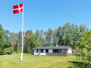 Una casa de un piso con asta de bandera, rodeada de un césped cuidado y árboles.