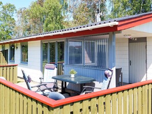 Een overdekt terras met een tafel en stoelen, een kleine potplant en een raam met zonwering.