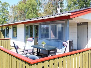 Een overdekt terras met een tafel, stoelen, een raam met zonwering en een deur.