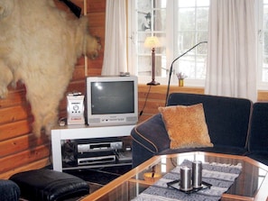 En stue med fjernsyn, sofa, sofabord i glas og et monteret trofædyr.