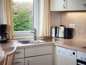 A modern kitchen with a stainless steel sink, a coffee maker, a kettle, and a dishwasher.